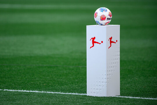 Soccer match ball displayed on a white pedestal with league-style icon on the pitch before kickoff, clean green background.