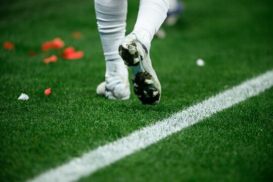 Lower body of a football player walking on the pitch, taped calves and cleats on wet grass during a professional match.