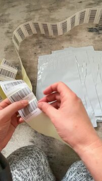 Moscow, Russia, 03.05.2026 Woman preparing shipment with barcode labels and poly mailer bags. Online shop seller organizing parcel packaging for delivery. Small business logistics process.