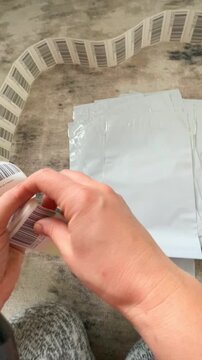 Moscow, Russia, 03.05.2026 Woman applying barcode label on plastic mailer bag. Small business seller preparing product for shipment. Logistics packaging process for online retail store.