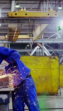 Vertical video: Worker grinding metal in factory, contacting grinder, finishing weld, sparks flying