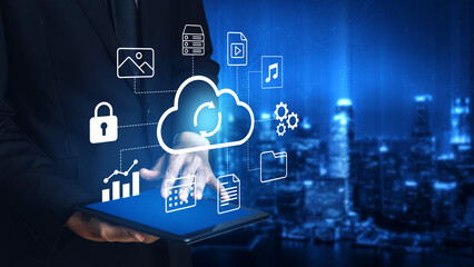 Obraz premium A businessman interacts with a tablet displaying cloud technology symbols, showcasing digital data management and security within a modern cityscape backdrop. Gantry