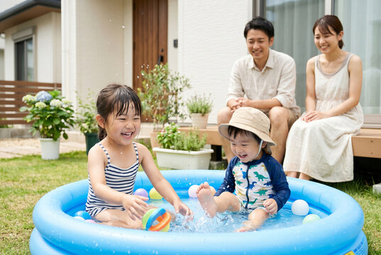夏の自宅の庭でビニールプール遊びを楽しむ子供たちと笑顔で見守る日本人家族 Generative AI