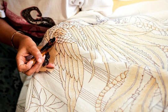 Artisan applying wax patterns on white fabric using a traditional canting. Focus on the organic movement and hand-eye coordination in authentic batik tulis production.