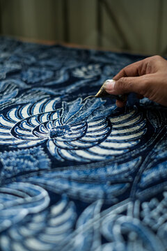 Detail shot of a copper canting tool tracing intricate floral patterns with melted wax on fabric. Showcasing the authentic precision of Indonesian batik tulis craftsmanship.