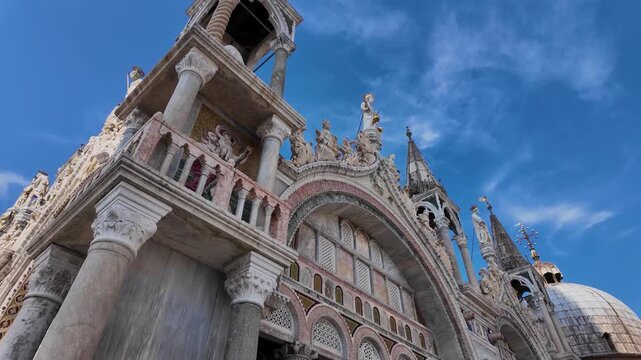 Dramatic upward exterior shot of St Mark's Basilica in Piazza San Marco, Venice, Italy showcasing ornate domes, arches, statues, and Byzantine architecture.