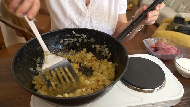 Close up of hands adding fresh raw partridge meat into a frying pan with caramelized onions. Traditional game meat recipe, gourmet cooking and artisan food preparation concept.