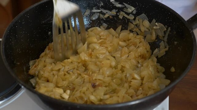 Close-up of hands using a spatula to saut&eacute; chopped onions in a pan. Soft natural lighting. Basic preparation for gourmet partridge p&acirc;t&eacute; or traditional Mediterranean recipes.