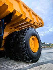 Low angle view of a giant yellow mining dump truck with massive tires, blue metal stairs and safety railings against dramatic cloudy blue sky. Heavy industrial mining vehicle concept. © Алина Неборская