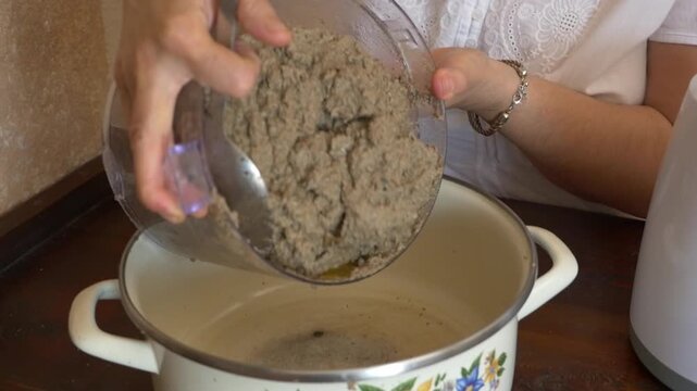 Medium shot of a woman's hands scraping homemade meat pate from a food processor and pouring it into a ceramic pot.