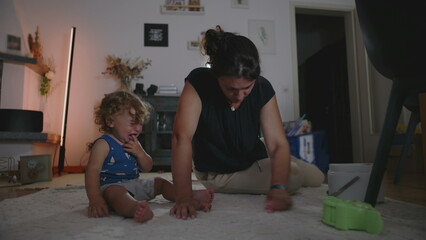 Naklejka premium Mother rubbing and cleaning carpet to remove a stain while toddler cries beside her seeking attention, candid indoor family moment showing daily parenting challenges