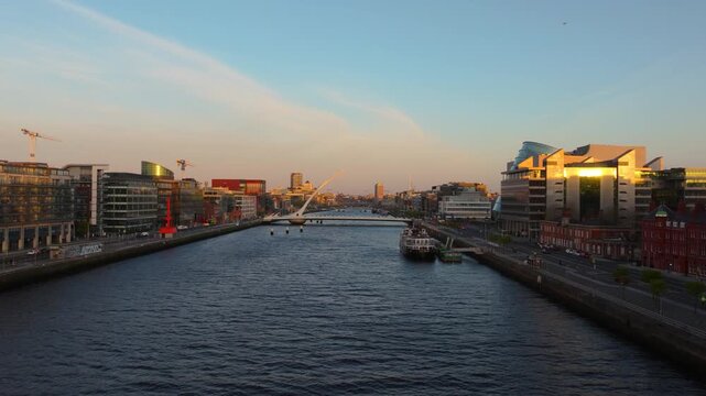 The sun rises over the River Liffey, illuminating Dublin's modern architecture and bridges. Ideal for cityscape visuals or urban development projects.