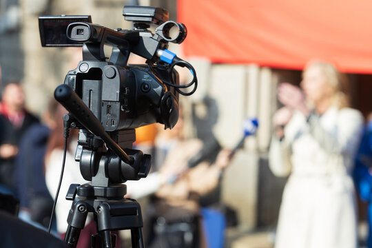 Professional video camera filming live outdoor media interview with reporter and microphone, media production and broadcast journalism concept