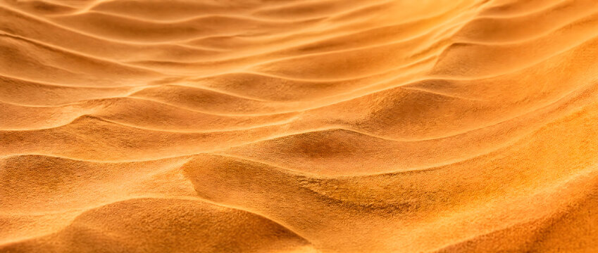 This close-up shot captures the soft, wind-formed wavy textures of golden desert sand dunes, showcasing warm tonal gradients and natural earthy patterns.