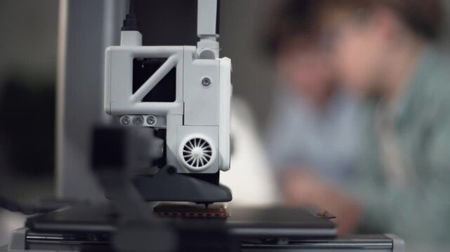 3D printer in operation in the foreground with kids on background