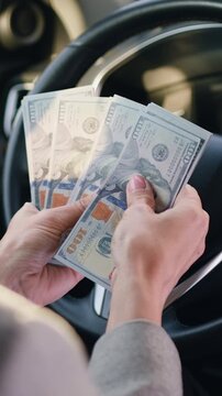 Close-up female hands behind steering wheel in luxury car counting cash financial profits in the parked car. Slow motion.