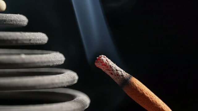Close up of smoking incense stick burning with soft smoke against a coiled incense or mosquito repellent background, creating a calming atmosphere