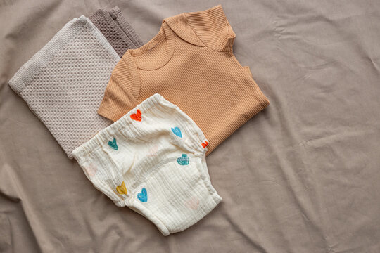 Beige baby bodysuit and white cotton diaper pantie and towels on on beige sheet, top view. Eco friendly cloth and accessories