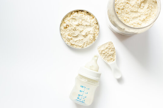 Baby milk bottle and powdered infant formula in the jar and scoop on white background. Top view.