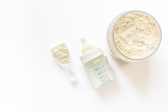 Baby milk bottle and powdered infant formula in the jar and scoop on white background. Top view.