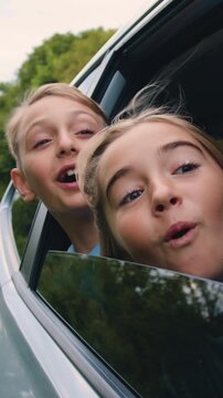 Carefree little children leaned out of the car window and smiled. Happy family enjoy and having fun together with outdoor lifestyle activity on road trip vacation. Slow motion.