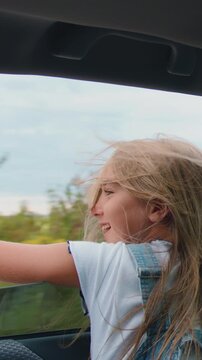 Back view. Happy child in car window. Little girl stretches her hand out of car window sun glare sunset. Slow motion.