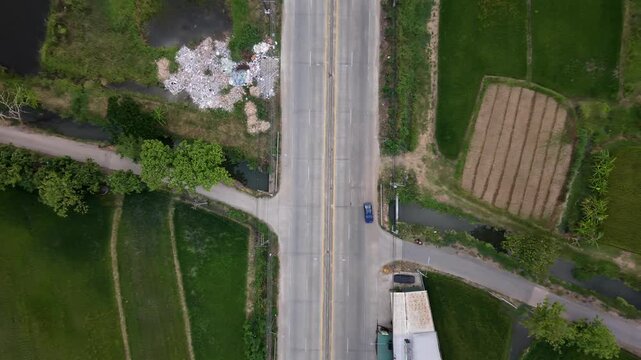 Professional 4K drone top-down view of a rural intersection surrounded by vibrant rice paddies and agricultural fields in a Southeast Asian setting.