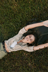 Naklejka premium Relaxed woman lying in tall grass, arms stretched above her head, enjoying a carefree outdoor moment. Natural light creates a warm, peaceful mood and wellness themes.