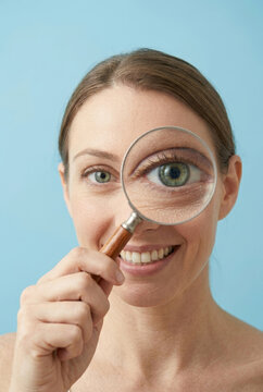 Woman holding magnifying glass in front of eye, enlarging eye. Searching for something, solving mystery and case.