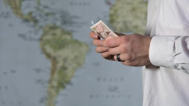 Close-up of a man's hands in a white shirt in profile counting money against a world map