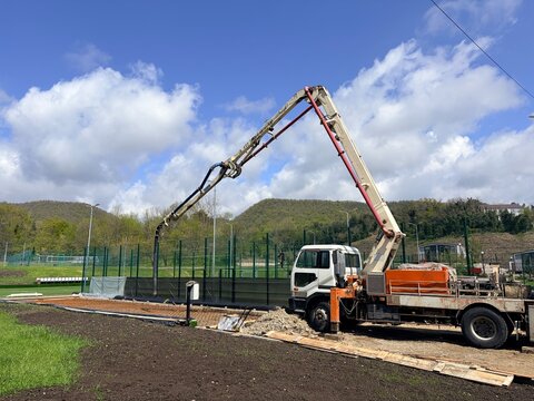 a construction scene featuring a large concrete pump truck with its articulated boom arm extended high into the air.
