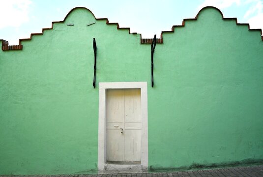 Typical Adobe house facade with a turquoise green stucco wall and a white wooden door in Atlixco, Puebla Mexico.
