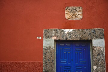 Naklejka premium Old Colonial house blue wooden door with stone trim on a Venetian red stucco wall in San Miguel de Allende, Guanajuato Mexico.