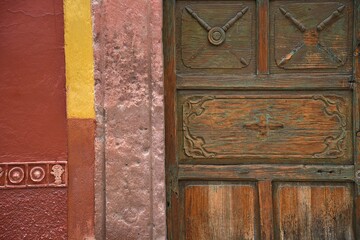 Fototapeta premium Old Colonial house facade with a Venetian stucco wall and an antique hand carved solid oak wooden door in San Miguel de Allende, Guanajuato Mexico.