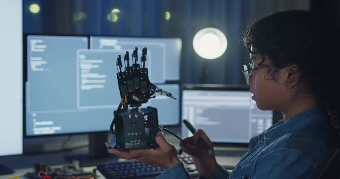 Young African American female programmer coding AI software on multiple screens in night office. Network security, cybersecurity, machine learning, working late, overtime, robotics automation concept.