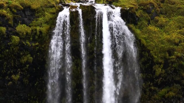 Close aerial drone shot flying along the falling water of Seljalandsfoss waterfall, detailed texture of the stream, dramatic cinematic nature scene with birds