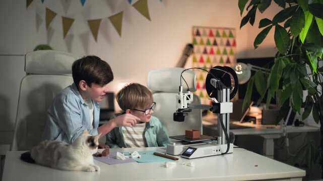 At a white table, two kids stop a 3D printer and take away the printed part