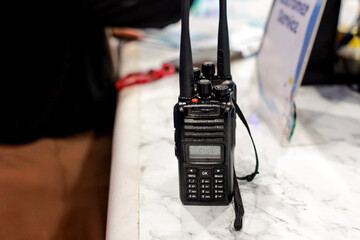 professional black handheld transceiver or walkie talkie sits upright on a white marble-patterned surface © awgraphoto