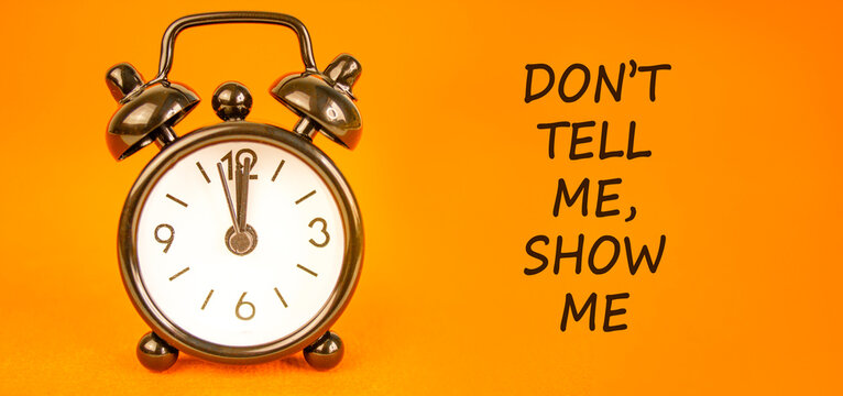 Tell or show symbol. Concept words Do not tell me, show me on beautiful orange paper. Beautiful orange paper background. Beautiful black alarm clock. Business tell or show concept. Copy space.