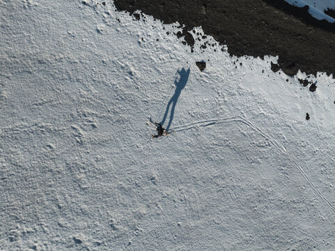 Aerial view of a person walking on the snow-covered south slope of Mount Etna with a long shadow and dark volcanic soil in Nicolosi, Sicilia, Italy.