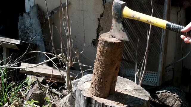 man splitting log with axe, wood flying as axe strikes log. Backyard scene with chopped wood and greenery, active motion, natural outdoor lifestyle, closeup detail of action. High quality 4k footage