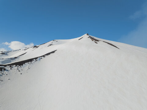 Aerial view of the snow-covered south slope of Mount Etna with volcanic rock ridges under a clear blue sky in Nicolosi, Sicilia, Italy.