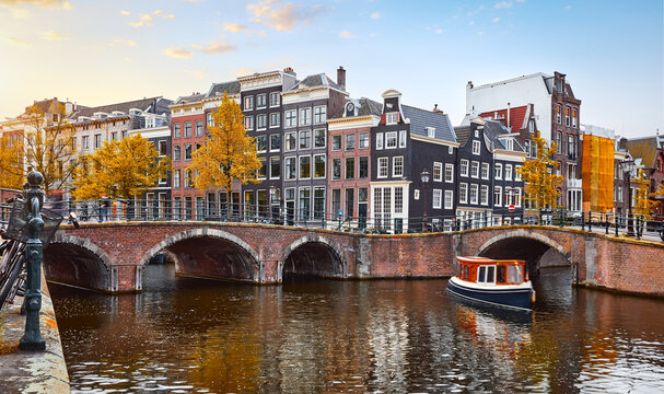 Amsterdam Netherlands. Traditional dancing houses on the river Amstel channel. Pleasure boat under the bridge. Sunset time. Popular travel destination in Europe