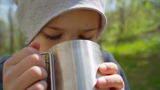 Close up of child face drinking tea from steel mug outdoors. Natural environment reduces stress and helps focus on basic senses and well being during travel.