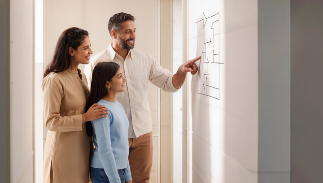 Family discussing renovation plans at home, parents and child looking at wall layout for interior design and home improvement planning