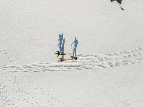 Aerial view of three skiers with long shadows trekking across the snow-covered slopes of Mount Etna south side in Nicolosi, Sicilia, Italy.