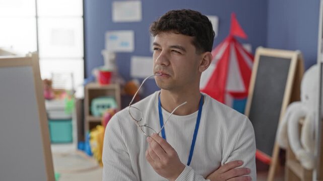 Man teacher holding glasses to mouth and arms crossed in a school building; thoughtful planning reflection.