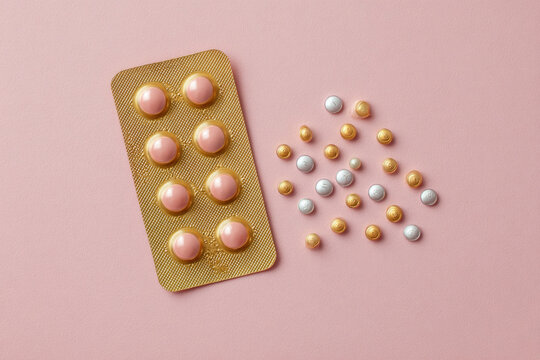 Hormonal oral contraceptives pills in a blister for a month of reception lie on pastel pink background. Flat lay, top view, copy space. 