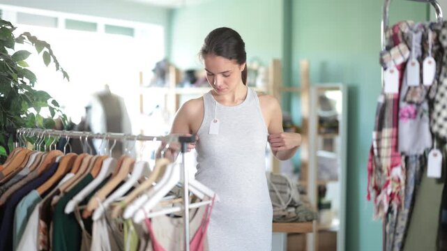 Young woman buyer trying on gray summer dress in clothing store