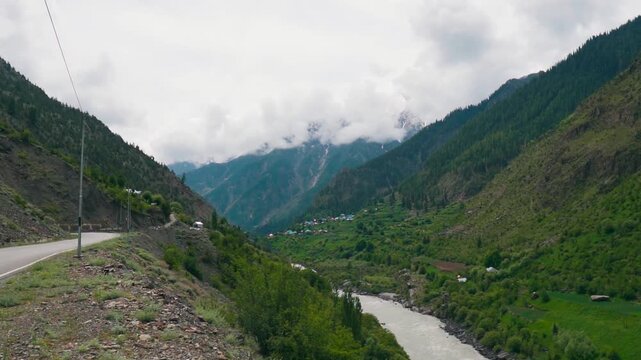 Wide angle shot of Chenab river flowing besides the Himalayan mountains during the summer season and mountain peaks covered by clouds as seen near Triloknath village in Lahaul, Himachal Pradesh, India